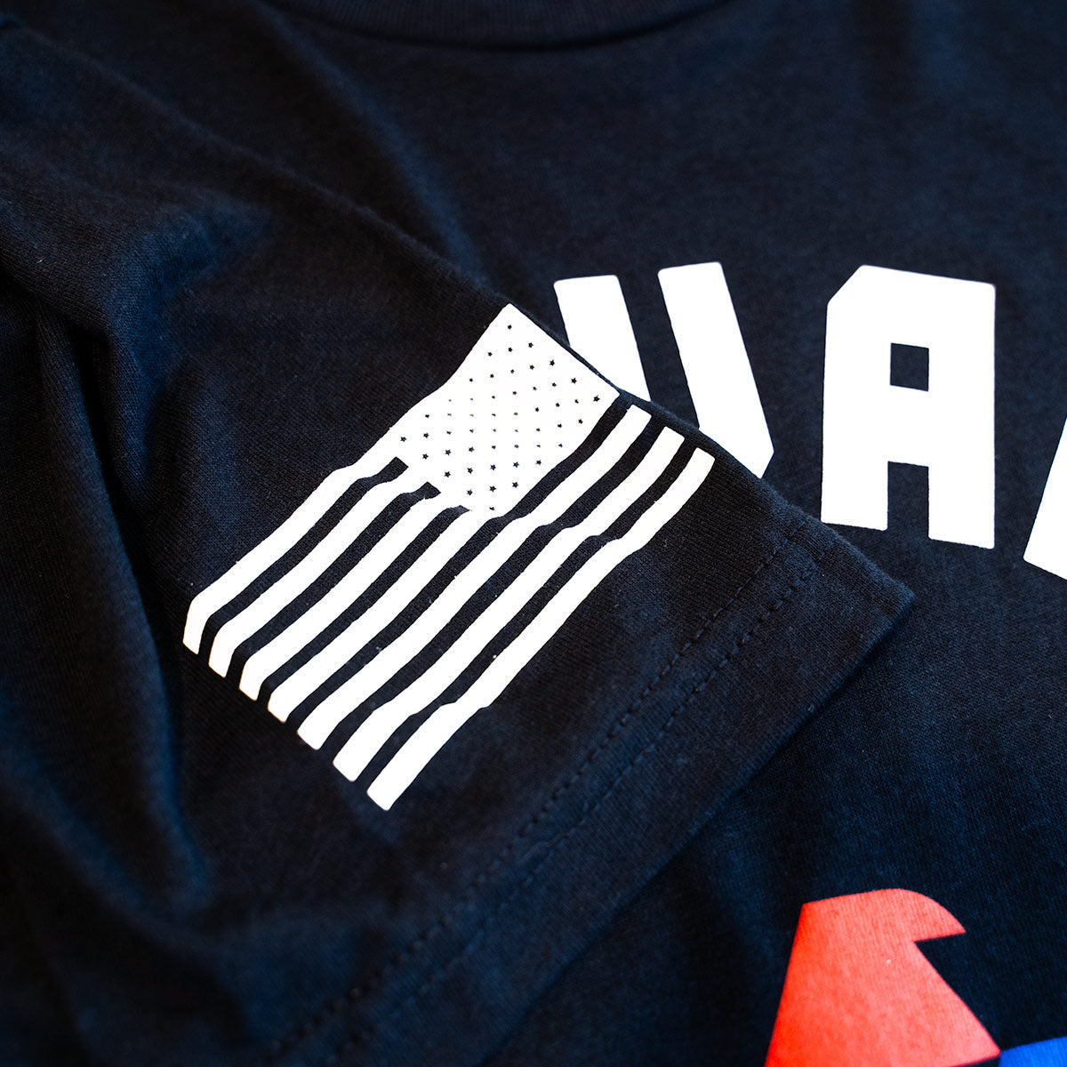 Black t-shirt with white graphic design and text on a dark background. American Flag on sleeve.